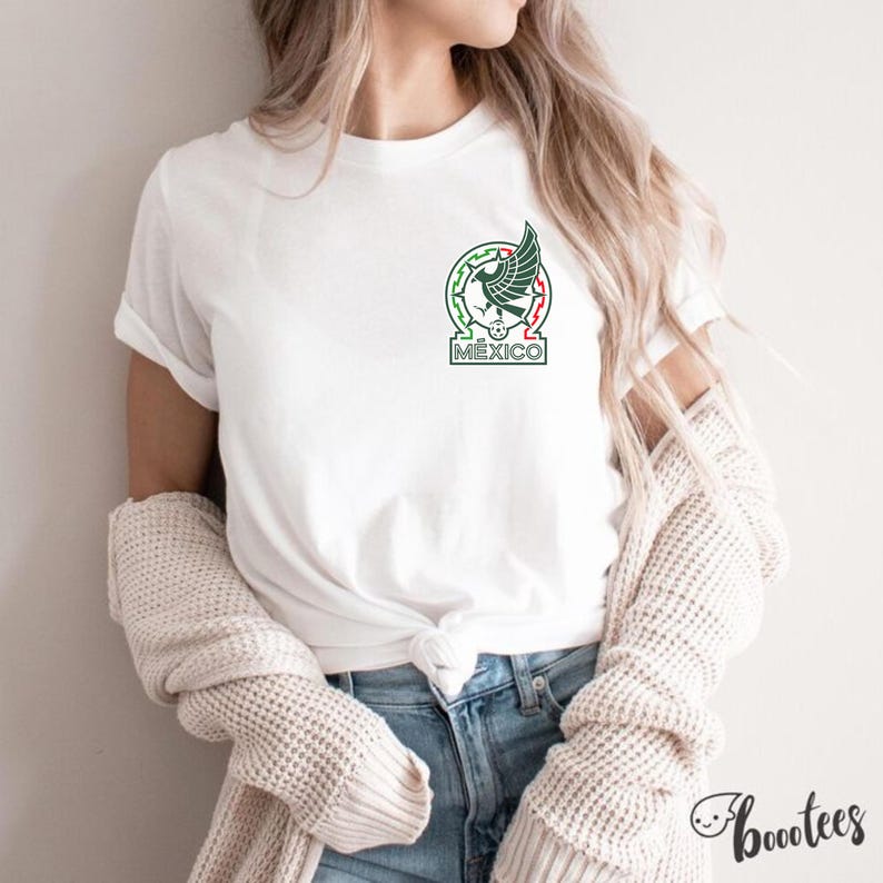 Peut inclure: T-shirt blanc avec les armoiries mexicaines, dans un design vert, rouge et blanc. Le t-shirt a un col rond et des manches courtes. Le mot "M&Eacute;XICO" est imprim&eacute; sous l'embl&egrave;me. Le t-shirt est port&eacute; avec un jean bleu.