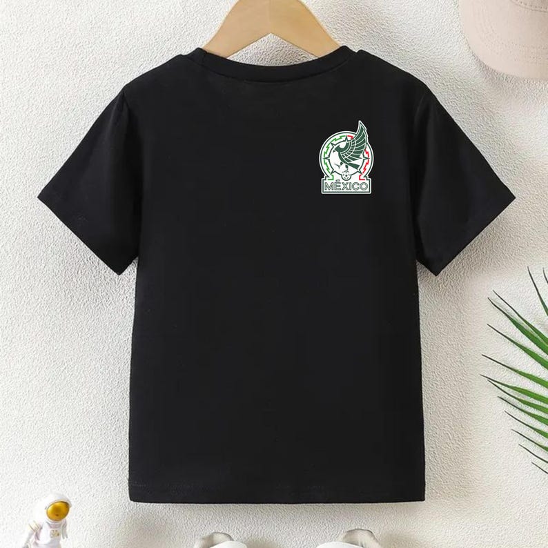 Peut inclure: T-shirt noir &agrave; manches courtes avec les armoiries mexicaines sur le haut de la poitrine gauche. L'embl&egrave;me repr&eacute;sente un aigle avec un serpent dans le bec, entour&eacute; d'une bordure verte et rouge, et le mot "MEXICO".