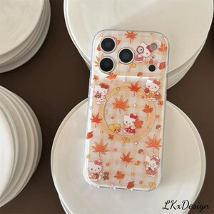 K&ouml;nnte beinhalten: Transparente Handyh&uuml;lle mit einem sich wiederholenden Muster aus Hello Kitty-Charakteren, Ahornbl&auml;ttern und Sternen in Orange und Wei&szlig;. Die H&uuml;lle hat einen transparenten Rand und einen kreisf&ouml;rmigen Ausschnitt. Das Design ist vor einem hellorange-wei&szlig; karierten Hintergrund angeordnet.