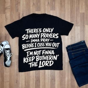 Puede incluir: Camiseta negra con texto blanco: "THERE'S ONLY SO MANY PRAYERS - IMMA PRAY - BEFORE I CUSS YOU OUT I'M NOT FINNA KEEP BOTHERIN' THE LORD." Incluye vaqueros azules y zapatillas deportivas blancas y negras. Ropa.