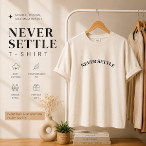 May include: Cream-colored t-shirt with the words "NEVER SETTLE" in black, hanging on a wooden hanger. The shirt is part of a minimalist design with text that reads "SOFT COTTON", "COMFORTABLE FIT", "UNISEX STYLE", and "PERFECT GIFT".