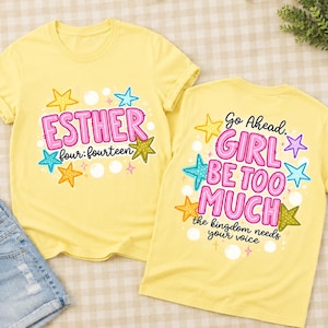 May include: Two light yellow t-shirts featuring colorful graphic designs. One shirt displays the text ESTHER four:fourteen in pink and black with yellow, blue, and green stars. The other shirt reads Go Ahead. GIRL BE TOO MUCH the kingdom needs your voice.