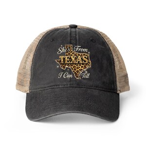 Może przedstawiać: Czarna czapka typu trucker z beżową siatką z tyłu. Przód przedstawia napis "She's From TEXAS I Can Tell" z obrysem Teksasu w panterkę.