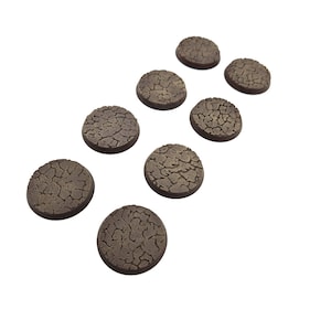 May include: A collection of nine brown, circular bases with a textured, cracked earth design. These miniature bases are ideal for tabletop gaming and model building, providing a detailed and realistic ground surface for figures.
