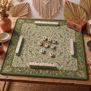 May include: A square mahjong mat featuring a detailed botanical pattern of green leaves, yellow flowers, and birds on a cream background. The mat has a dark green border and is set with several mahjong tiles arranged in rows and scattered in the centre.