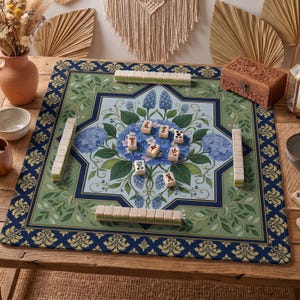 May include: A Mahjong game set on a wooden table. The game board has a floral design with blue hydrangeas and green leaves. The tiles are beige with black symbols. A wooden box and other decorative items are also present.