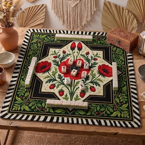 May include: A decorative Mahjong game set on a wooden table. The game board features a floral design with red poppies and green foliage. The border is black with a striped pattern. Mahjong tiles are arranged on the board.
