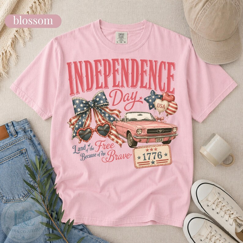 K&ouml;nnte beinhalten: Hellrosa Independence Day T-Shirt mit einem Aufdruck eines Oldtimer-Cabrios in Rosa, herzf&ouml;rmigen Sonnenbrillen und einer patriotischen Schleife. Das Shirt tr&auml;gt den Text "Independence Day" und "Land of the Free Because of the Brave."