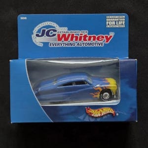 Peut inclure: Une voiture miniature Hot Wheels bleue avec des flammes jaunes et oranges à l'avant, présentée dans une boîte bleue JC Whitney. La boîte porte l'inscription "EVERYTHING AUTOMOTIVE" et "Hot Wheels".