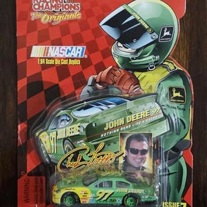 May include: A Racing Champions die-cast replica of a NASCAR John Deere race car. The packaging features a green and yellow car with the number 97, a driver image, and the text "John Deere". The packaging also includes the text "The Originals".