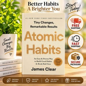 May include: A hardcover book titled Atomic Habits by James Clear with a cream cover and gold text. The book is positioned next to a white planter with the text Small Changes Big Results and a stack of three books labeled Healthier You, Happier You, Brighter Future.