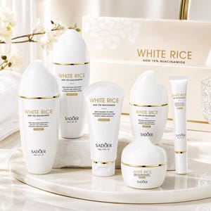 May include: A collection of white skincare products with gold accents, including bottles, tubes, and a jar. The products are labeled "WHITE RICE ADD 15% NIACINAMIDE" and "SADOER". The set includes toner, lotion, cleanser, serum, and cream.