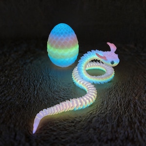 May include: A luminous, articulated snake toy and an egg-shaped object. The snake is white with blue, yellow, and pink accents. The egg is blue, green, and pink. Both items appear to glow, creating a fantasy theme.