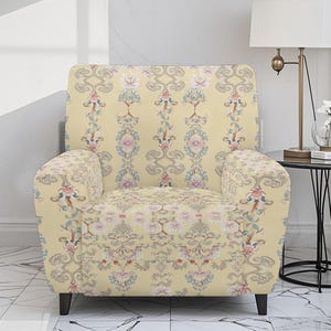 May include: A cream-colored armchair with a floral pattern in pink, blue, and green. The pattern is a repeating design of stylized flowers and leaves. The chair has black legs and a classic silhouette.