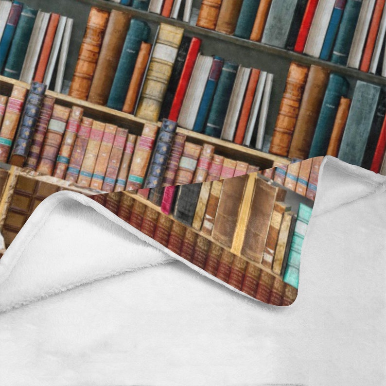 Pode incluir: Um cobertor branco com um design estampado de uma estante de livros cheia de filas de livros antigos encadernados em couro com lombadas coloridas.