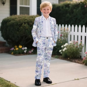 May include: A floral print suit for a child, featuring a white button-down shirt, a jacket, and matching pants. The suit has a light blue and purple floral pattern. The child is wearing black dress shoes.