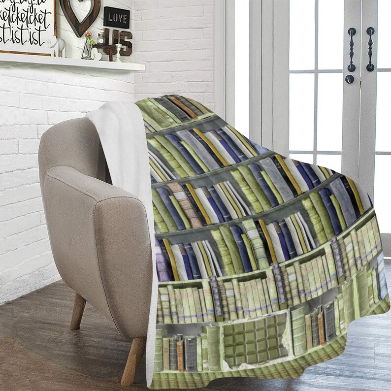 Pode incluir: Uma manta macia e felpuda com um design estampado de uma estante cheia de livros. A manta &eacute; de cor castanho claro com uma borda branca.