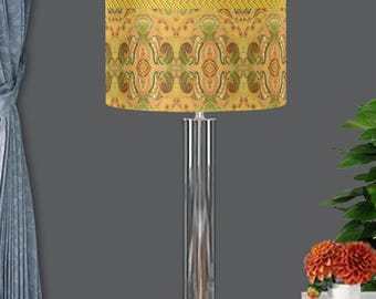 May include: A table lamp with a gold and green patterned lampshade and a clear glass base. The lampshade has a gold and pink trim.