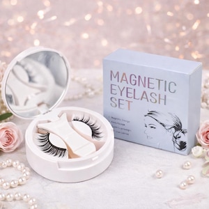May include: A white magnetic eyelash set with a mirror and a box. The box reads "MAGNETIC EYELASH SET" with a woman's silhouette. The set includes a pair of black eyelashes and an applicator. The background has pearls and pink flowers.