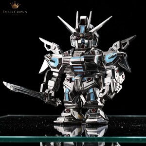 May include: A white ceramic mug with a black handle and the text "But First, Coffee" in a bold, black font. The mug is set against a blurred background, suggesting a cozy setting.