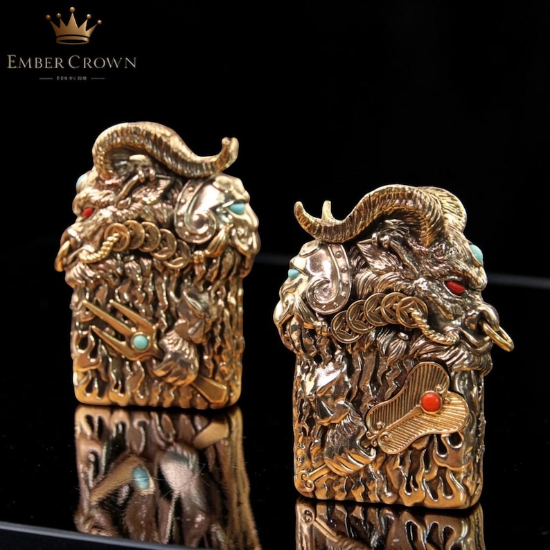 K&ouml;nnte beinhalten: Zwei verzierte, goldfarbene Metallskulpturen von Widderk&ouml;pfen mit gebogenen H&ouml;rnern, roten Augen und t&uuml;rkisen und roten Akzenten. Die Skulpturen weisen komplizierte Details auf und sind vor einem dunklen Hintergrund platziert. Der Text "EMBER CROWN" befindet sich oben links.