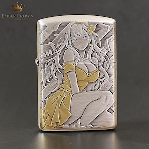 Puede incluir: Un encendedor de metal plateado con una ilustraci&oacute;n grabada de estilo anime de una mujer con un vestido amarillo. El encendedor tiene un acabado de metal cepillado y la marca "EMBER CROWN" es visible en la parte superior izquierda.