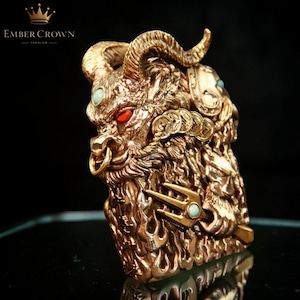 K&ouml;nnte beinhalten: Eine detaillierte, goldfarbene Skulptur einer bullenartigen Kreatur mit roten Augen und t&uuml;rkisfarbenen Akzenten. Die Skulptur weist komplizierte Details wie H&ouml;rner, M&uuml;nzen und einen Dreizack auf. Das Ember Crown-Logo ist sichtbar.