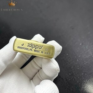 Puede incluir: Un encendedor Zippo de color lat&oacute;n con el texto "Zippo BRADFORD, PA. MADE IN U.S.A." y el n&uacute;mero "22" grabado en la superficie. El encendedor es rectangular con bordes redondeados.