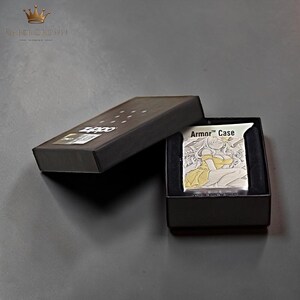 Puede incluir: Un encendedor Armor Case plateado con una ilustraci&oacute;n de estilo anime amarillo y blanco, presentado en una caja negra. La caja est&aacute; abierta, revelando el encendedor y su estuche protector. El encendedor presenta el texto "Armor Case".