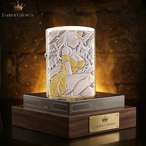 Puede incluir: Un encendedor plateado y dorado con una ilustraci&oacute;n grabada de estilo anime de una mujer con un vestido amarillo. El encendedor se exhibe en una caja de madera con el texto "EMBER CROWN".