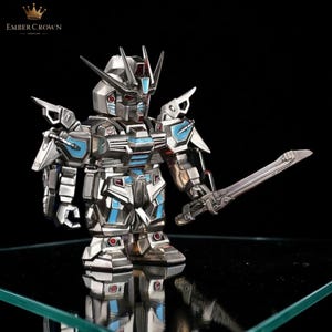 May include: A silver and blue robot figurine with a sword. The robot has a detailed design with blue accents and red details. The Ember Crown logo is in the top left corner.
