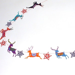 May include: A decorative garland featuring a series of colorful reindeer and star-shaped cutouts strung together on a thin cord. The reindeer are depicted in various poses and colors, including orange, purple, blue, and teal, with intricate patterns.