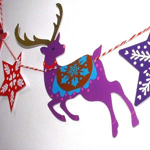 May include: A decorative garland featuring a purple reindeer with gold antlers and a blue and brown snowflake saddle, flanked by a red star with white heart patterns and a purple star with white snowflake designs, all strung on red and white twine.