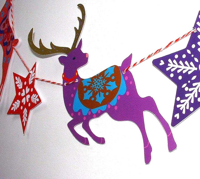 May include: A decorative garland featuring a purple reindeer with gold antlers and a blue and brown snowflake saddle, flanked by a red star with white heart patterns and a purple star with white snowflake designs, all strung on red and white twine.