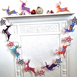 May include: A decorative garland featuring alternating cutouts of leaping reindeer and stars in vibrant colors including red, blue, purple, and orange. The reindeer and stars are connected by a thin string, creating a festive hanging display.