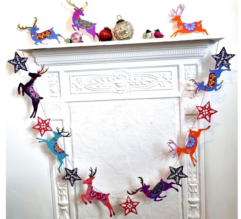 May include: A decorative garland featuring alternating cutouts of leaping reindeer and stars in vibrant colors including red, blue, purple, and orange. The reindeer and stars are connected by a thin string, creating a festive hanging display.