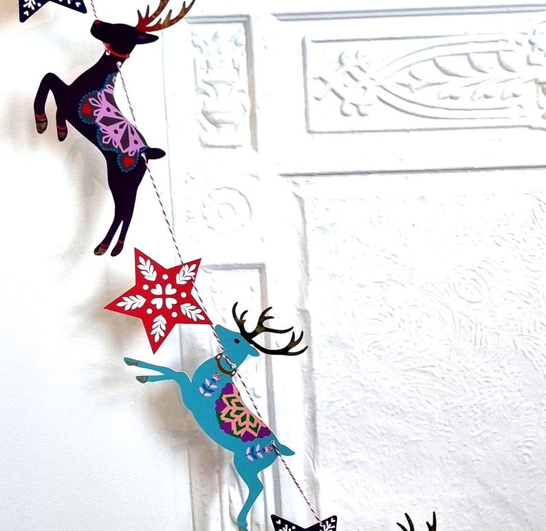 May include: A decorative garland featuring alternating cutouts of leaping reindeer and stars. The reindeer are colored in dark purple and bright blue with intricate floral patterns, while the stars are red with white snowflake-like designs.