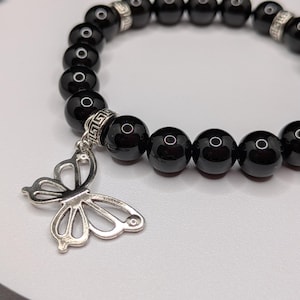 May include: A black beaded bracelet with a silver butterfly charm. The bracelet has large, round, glossy black beads and silver accent beads. The butterfly charm has openwork wings.