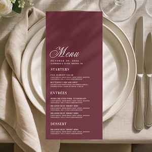 May include: A tall, rectangular menu card in deep burgundy with white text. The header reads Menu, October 30, 2026, Katherine & Peter, Boston, MA. It lists Starters, Entrees, and Dessert sections with detailed food descriptions in a serif font.