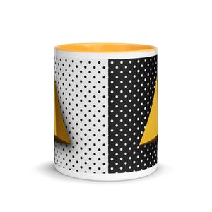 Könnte beinhalten: Ein Keramikbecher mit einem geteilten Design, das links einen weißen Hintergrund mit schwarzen Punkten und rechts einen schwarzen Hintergrund mit weißen Punkten aufweist. Das Innere des Bechers ist einfarbig gelb und ein gelbes Dreieck ist sichtbar.