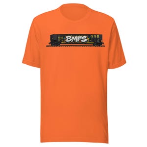 May include: Orange t-shirt featuring a graphic of a black freight train car with the text "BMFS" in graffiti style. The train car has the CSX logo and other markings. The shirt is a short-sleeved crew neck.