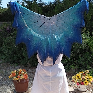 Peut inclure: Un châle bleu et turquoise est présenté contre un ciel ensoleillé. Le châle présente un effet dégradé, passant d'un bleu profond à un turquoise plus clair. Le châle a la forme d'un papillon ou d'une aile. La personne porte une robe blanche.