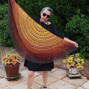 Peut inclure: Un châle en crochet aux tons marron, orange et jaune est présenté, mettant en valeur son design ajouré complexe. Le châle a un bord festonné et est présenté en extérieur.