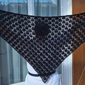 Peut inclure: Un châle triangulaire noir au crochet avec un motif en losanges. Le châle est maintenu, mettant en valeur son tissage ajouré et son design complexe. Les bords sont finis avec une bordure décorative et des liens.