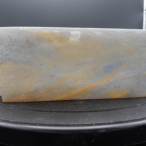 May include: A rectangular, translucent container with a marbled effect. The colors include gray, gold, and blue, creating a unique, artistic appearance. The container is likely used for decorative purposes.