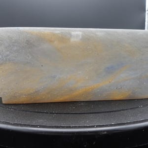 May include: A rectangular stone planter with rounded corners, featuring a smooth, translucent surface with swirling patterns of muted gray, soft blue, and warm golden-yellow hues. The base has small, notched cutouts on the bottom corners.