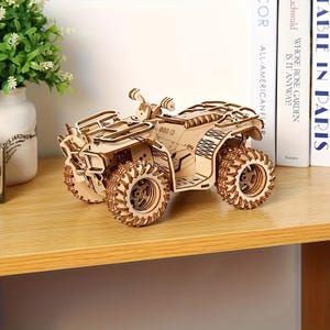 May include: A wooden ATV model with intricate details, including large, textured wheels and a detailed frame. The model is made of light-colored wood and sits on a wooden surface. The text "800 G" is visible on the model.