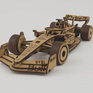 以下が含まれることがあります： 木製のF1レーシングカーの模型。車は明るい茶色の木材と濃い茶色の車輪でできています。モデルには、スポンサーロゴや「BYBL」と「Mobil」のテキストなど、詳細な機能があります。