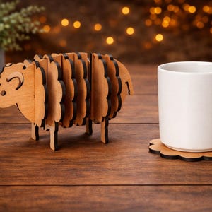 May include: A wooden sheep-shaped decorative item with a white mug and a flower-shaped coaster on a wooden surface. The sheep is made of layered wood with a light brown color and dark brown edges. A potted plant is in the background.