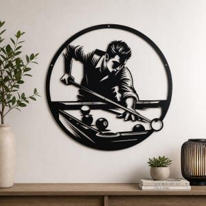 Puede incluir: Arte de pared de metal negro que representa a una persona jugando al billar, enmarcado en un círculo. La obra de arte muestra a un jugador apuntando con un taco a las bolas de billar sobre una mesa. El diseño es una silueta, adecuada para la decoración del hogar.